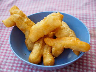 Closeup detail of Pa Thong Ko, also known as Chinese fried crullers, in a blue bowl on red tablecloth at a street vendor. Chiang Rai, Thailand. Travel and cuisine.