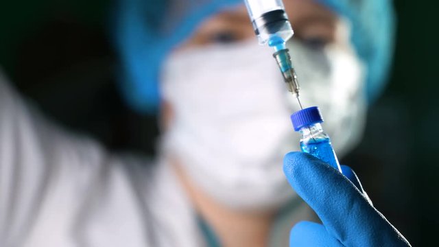 Female doctor picking up medication into a syringe and prepares it for injection.