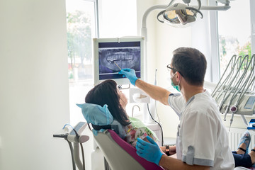 Doctor dentist showing patient's teeth on X-ray - obrazy, fototapety, plakaty