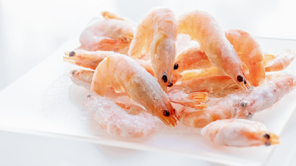 Shrimps lie on a small glass transparent plate on a bright table