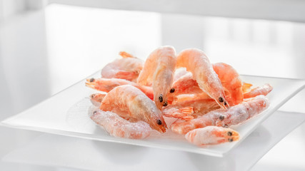 Shrimps lie on a small glass transparent plate on a bright table
