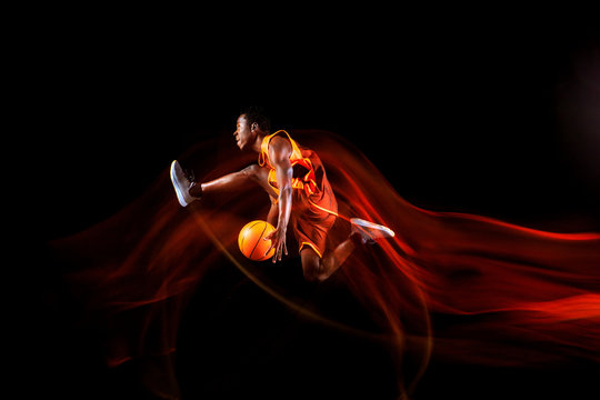 Fly over the Earth. African-american young basketball player of red team in action and neon lights over dark studio background. Concept of sport, movement, energy and dynamic, healthy lifestyle.