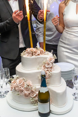 Three-tiered white wedding cake with sparklers and champagne on restaurant table ready for bride and groom