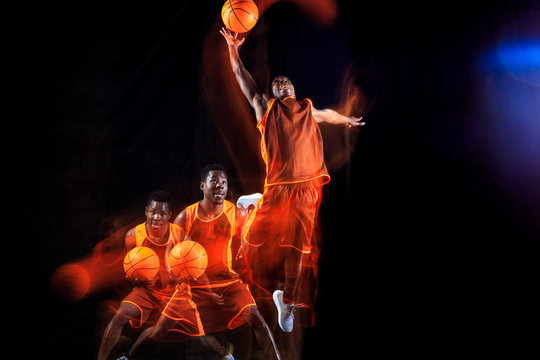 Higher than sky. African-american young basketball player of red team in action and neon lights over dark studio background. Concept of sport, movement, energy and dynamic, healthy lifestyle.