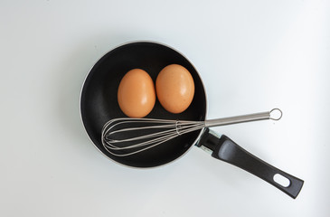 Pan with egg and stainless steel egg whisk on the white background