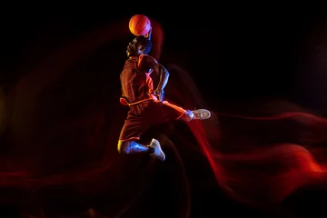 Fotobehang One moment to win. African-american young basketball player of red team in action and neon lights over dark studio background. Concept of sport, movement, energy and dynamic, healthy lifestyle. © master1305