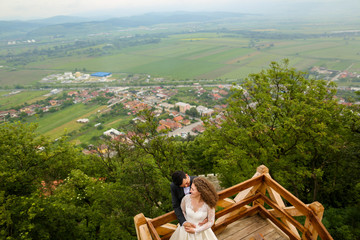 Beautiful wedding couple posing on hill with view of village