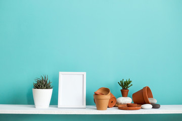 White shelf against pastel turquoise wall with pottery and succulent plant with potted succulent plant.