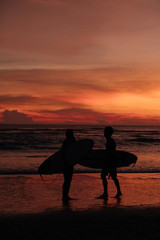 Surfers silhouette walking across the sea shore at sunset
