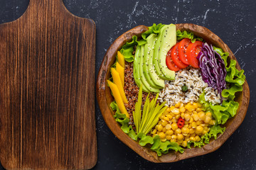 Healthy vegan superfood bowl with quinoa, wild rice, chickpea, tomatoes, avocado, greens, cabbage, lettuce on black stone background with cutting board, top view with copy space. Food and health