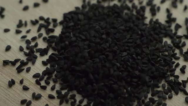 Cumin seeds falls on the wooden rotating board; close up, macro shot; slow motion.