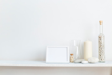 Obraz na płótnie Canvas Shelf against white wall with decorative candle, glass and rocks.