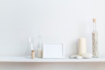 Fototapeta na wymiar Shelf against white wall with decorative candle, glass and rocks.
