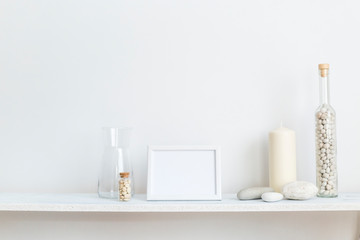 Fototapeta na wymiar Shelf against white wall with decorative candle, glass and rocks.