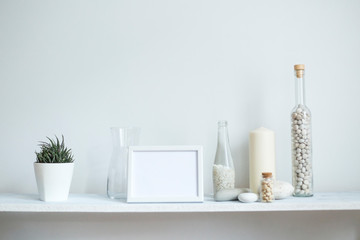 Fototapeta na wymiar Shelf against white wall with decorative candle, glass and rocks. Potted succulent plant.
