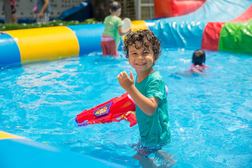 Cute boy playing in the swimming pool with water gun. Summer time. 