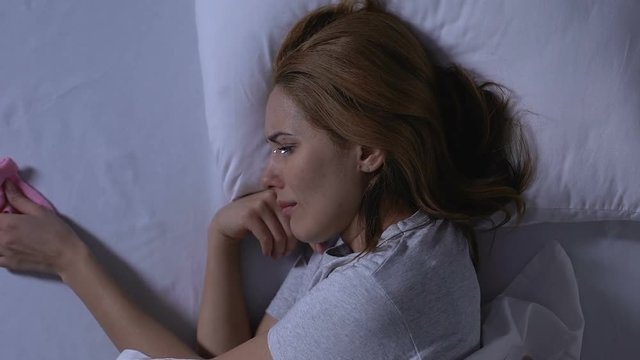 Crying lady lying in bed, holding pink baby socks, depression after misbirth