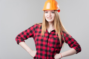 Portrait of a young attractive woman with blond hair in orange helmet on a neutral gray background.