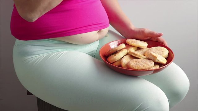 sitting hungry obese woman with fat stomach eat cookies  close up .food addiction gluttony concept