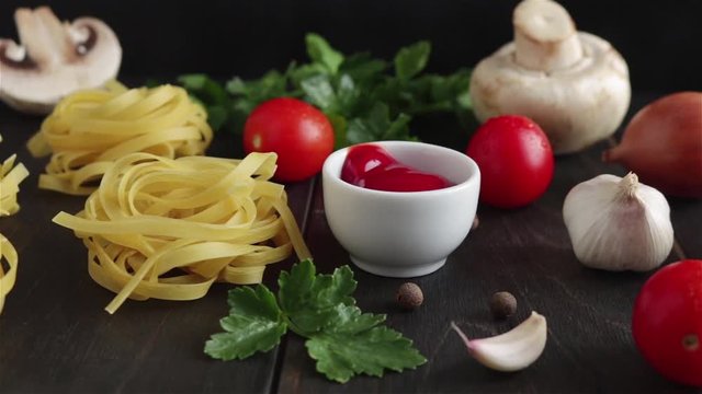 pasta ingredients on wooden table  panning shot.raw fettuccine cherry tomatoes garlic mushrooms parsley