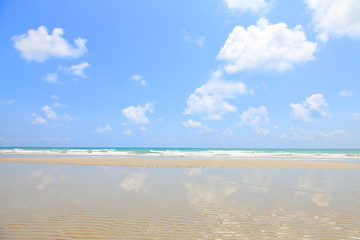 Sunny day at the beach with sand ripple texture on the bright blue sky and white cloud reflected on the sea with copy space