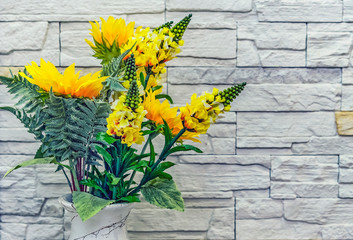 Bouquet of yellow artificial flowers on a stone wall background.