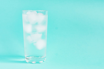 Close up of pure water with ice in tall transparent glass with copy space on blue  background.