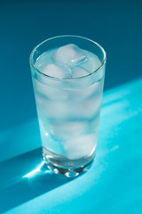 Close up of pure water with ice and paper straw in transparent glass and sun glare on blue  background.