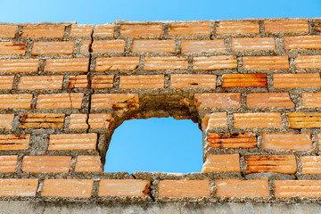 Close up hole of old outdoor orange brick wall with clear blue sky on background.