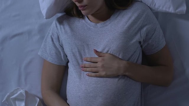Pregnant woman holding tummy and turning in bed, uncomfortable sleeping