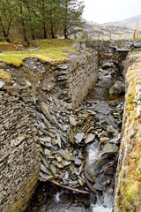Fototapeta na wymiar Stream trough reinforced by rocks on the Cwmorthin Waterfall trail in the mountains of Snowdonia National Park, Wales.