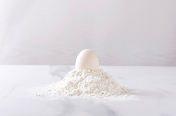 One egg on the heap of flour on the kithen whit table.Ingredients for baking products