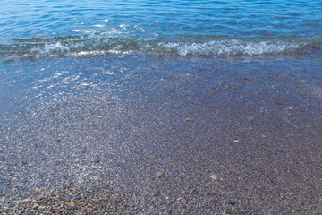 The texture of the crystal wave washing the small pebbles on the beach, selective focus