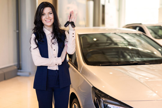 Happy woman buyer possing with keys near her new vehicle in car dealership
