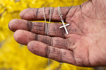 Silver cross in dirty hand of homeless elderly man on yellow background..Salvation of man, help, faith in Jesus, Holy Easter.