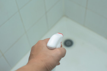 Hand hold the cleaning spray to clean the tile in the shower room