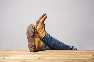lazy person concept: man's legs wearing  blue jeans  of desert boots rest on a wooden table with...
