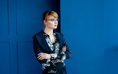 a young girl in strict clothes stands near the window and looks out the window 