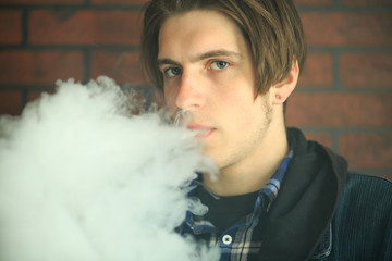 Vape teenager. Portrait of young handsome guy smoking an electronic cigarette in the bar. Bad habit...