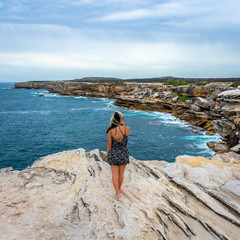Young girl looking at the sea from a rock cliff