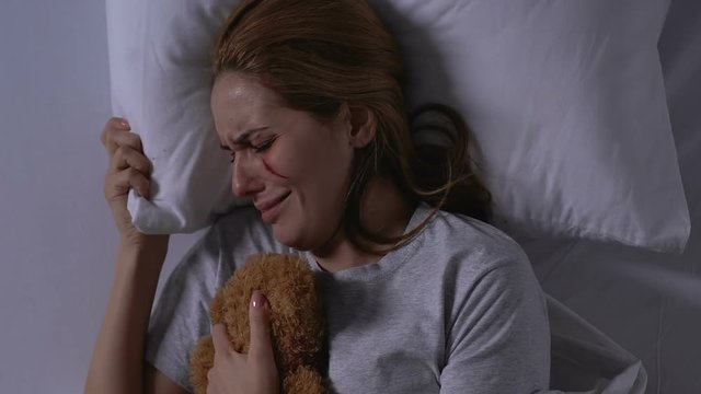 Lady with wounded face hugging teddy bear, crying in bed, victim needs support
