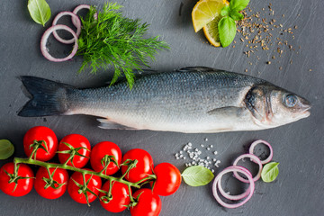 Raw seabass fish with ingredients for cooking a hot dish, top view