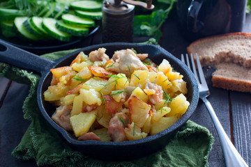 Fried potatoes with chicken on a cast-iron black frying pan, horizontal