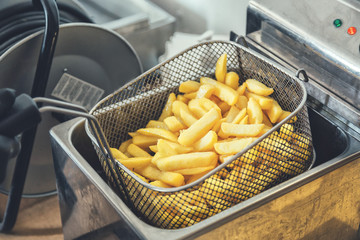 French fries cooking. Grid with strips of potato lowered into boiling oil. The concept of fast food. Belgian frit