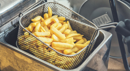 French fries cooking. Grid with strips of potato lowered into boiling oil. The concept of fast food. Belgian frit
