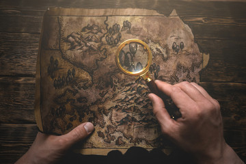 Traveler is looking on an old map in his hands through a magnifying glass. Treasure hunt concept.o