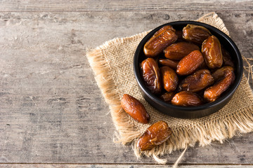 Dates in black bowl on wooden table. Copyspace