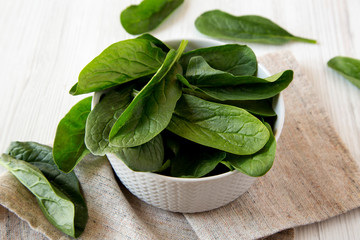 Raw spinach in a bowl over white wooden surface, side view. Close-up.