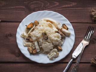 Hot breakfast of rice and seafood on a white plate on a rustic board in a rustic style tray, cutlery. Shot from close range.