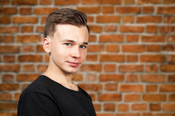 smiling portrait white young guy model dressed in black t-shirt looking at the camera on brick wall background